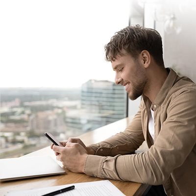 Ein Mann sitzt in einem Café am Fenster, lächelt und schaut auf sein Smartphone.